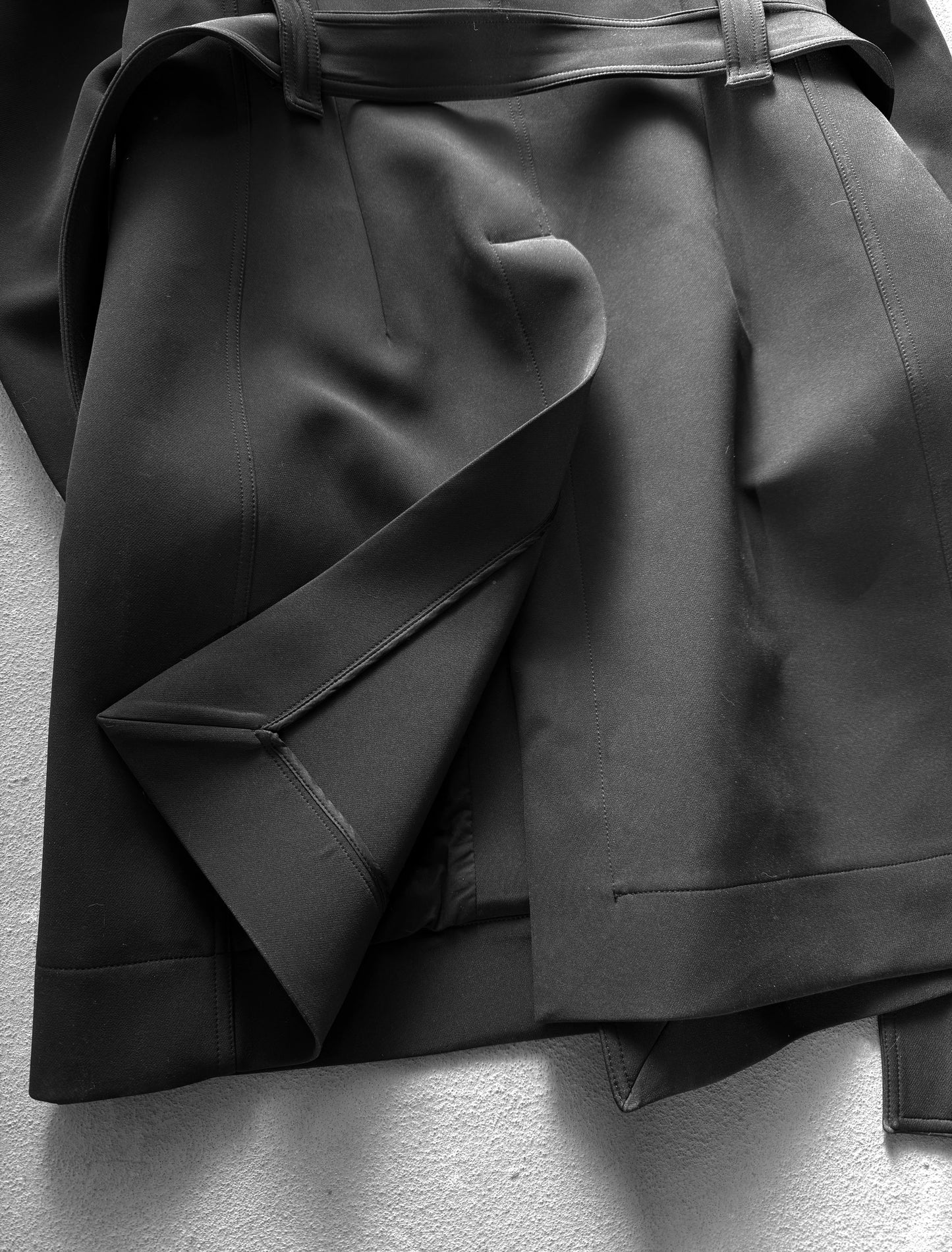 Close-up of a black coat with a belt on a light gray background