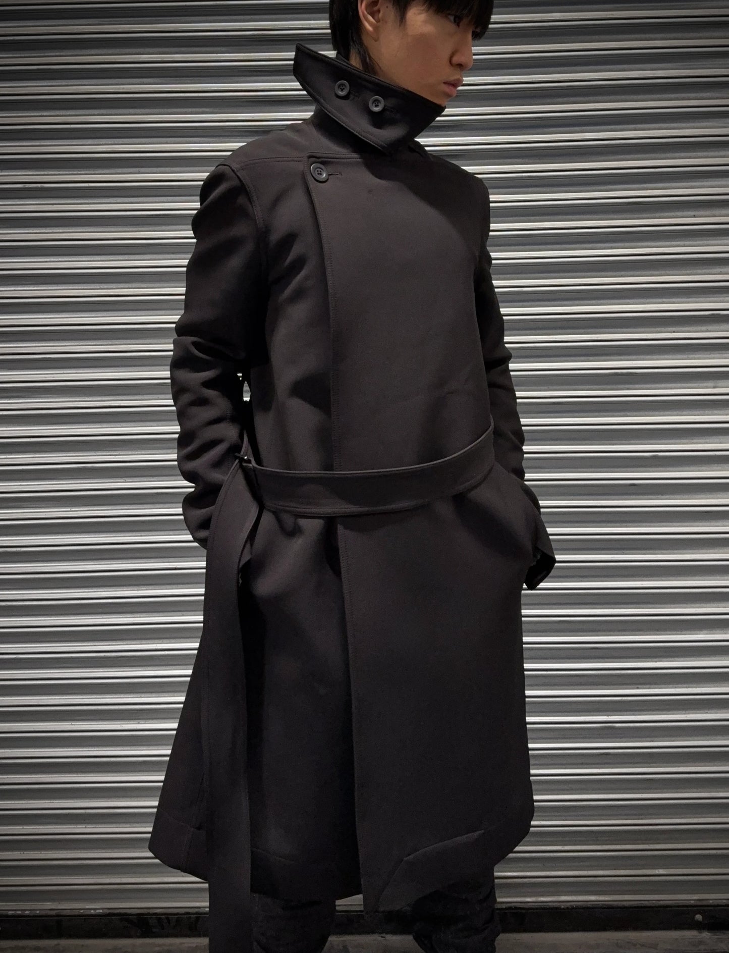 Person wearing a dark coat standing in front of a metallic shutter.