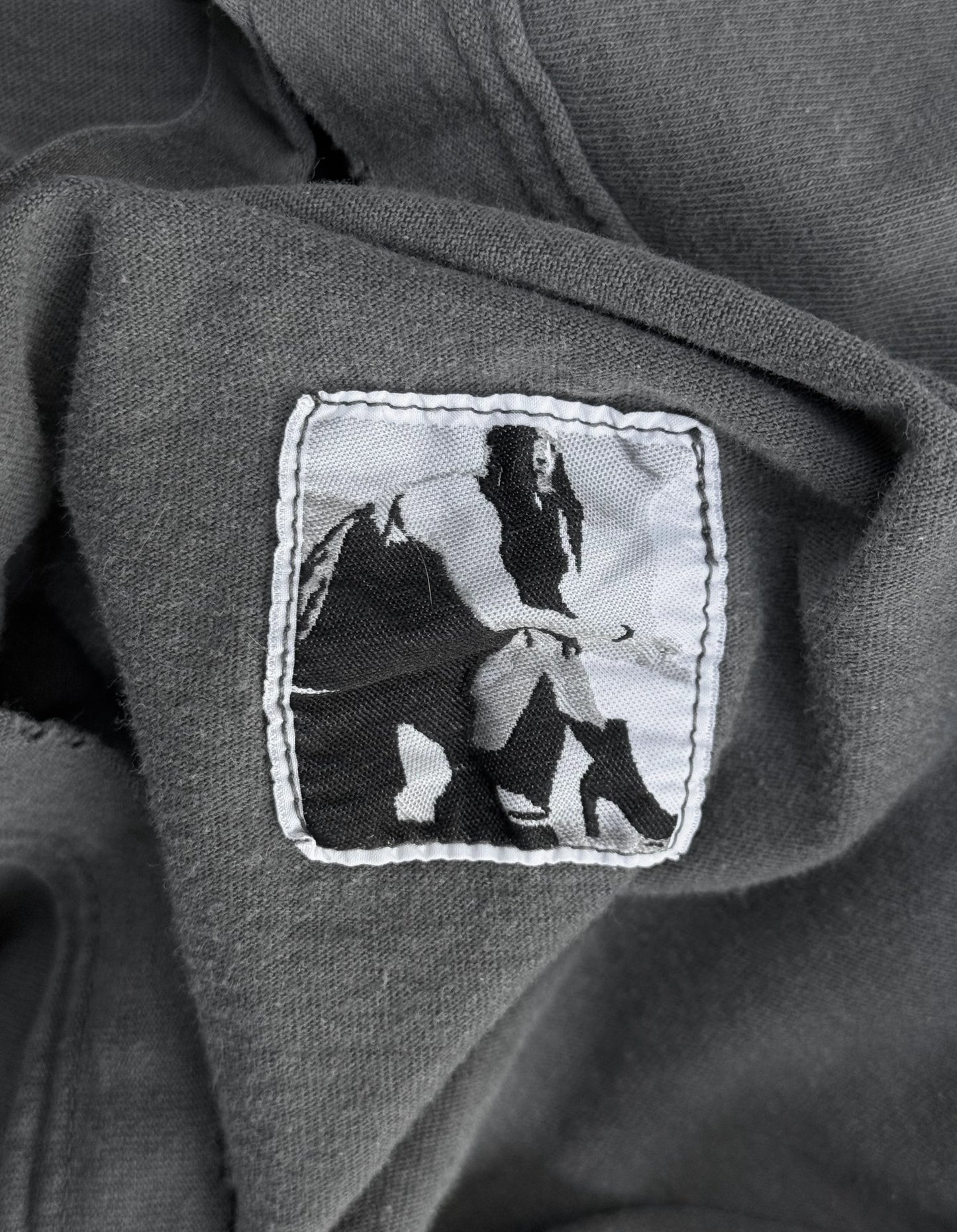 Patch on a dark fabric with a black and white design of a person holding a spear.