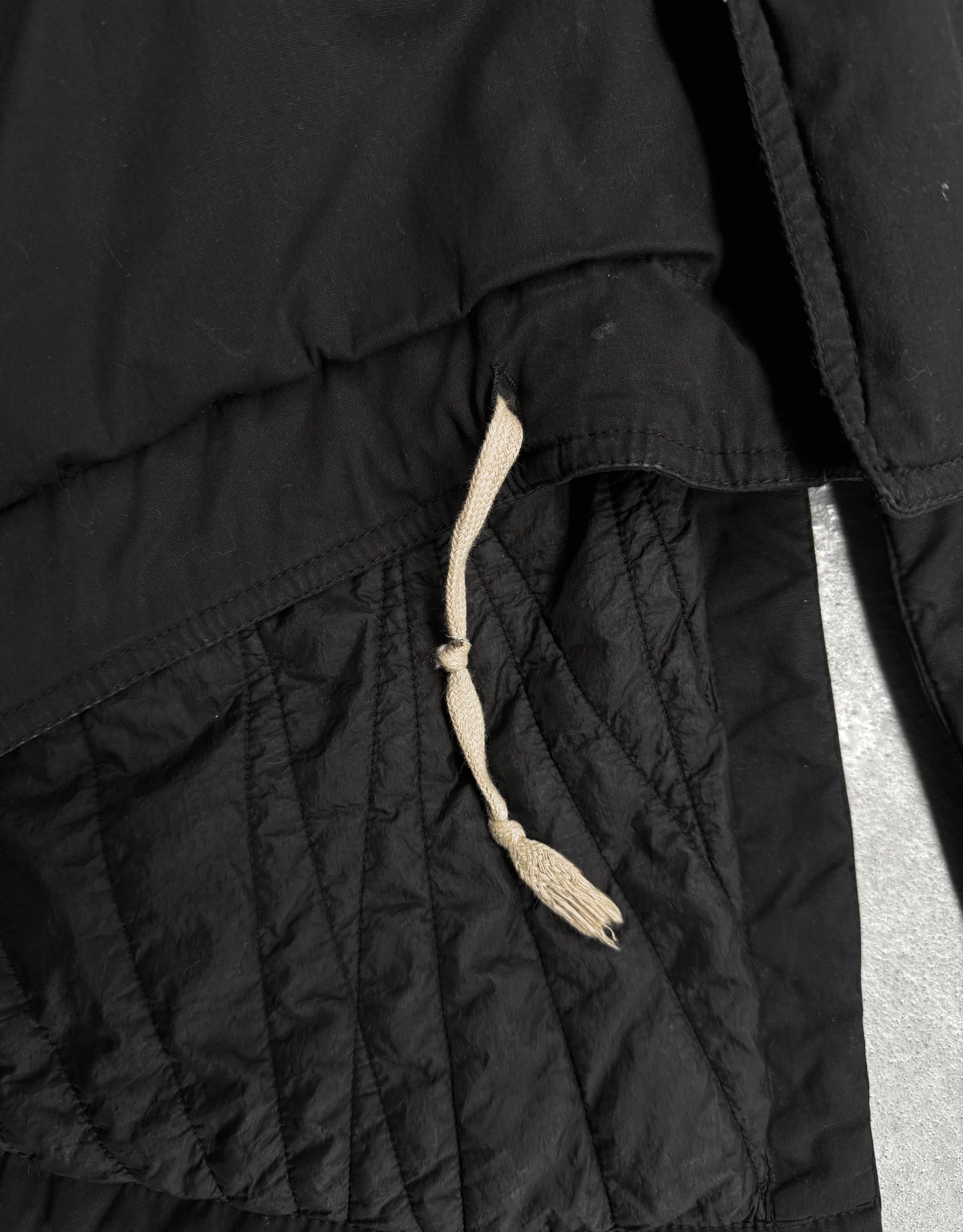 Close-up of a black quilted jacket with a drawstring on a light gray background