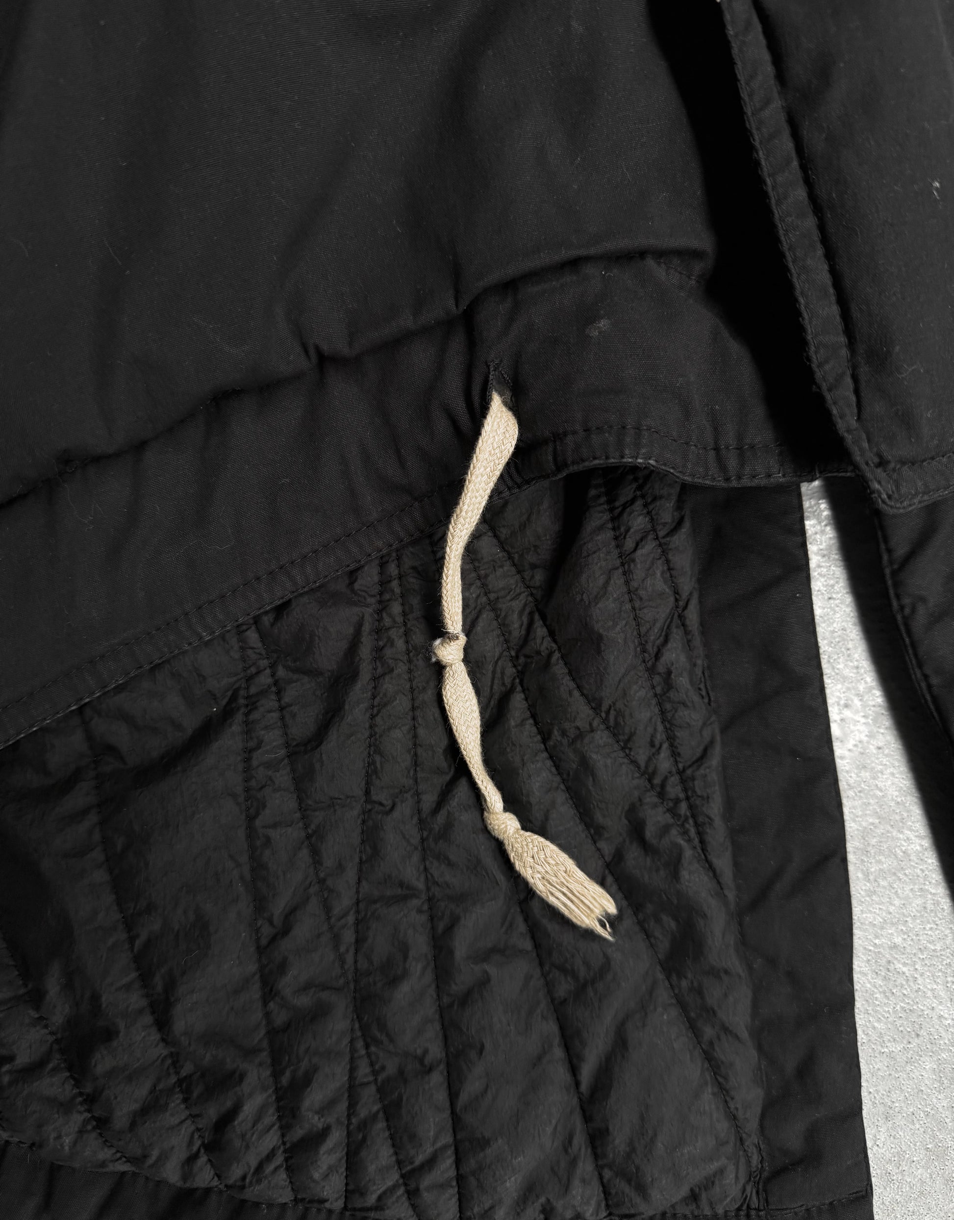 Close-up of a black quilted jacket with a drawstring on a light gray background