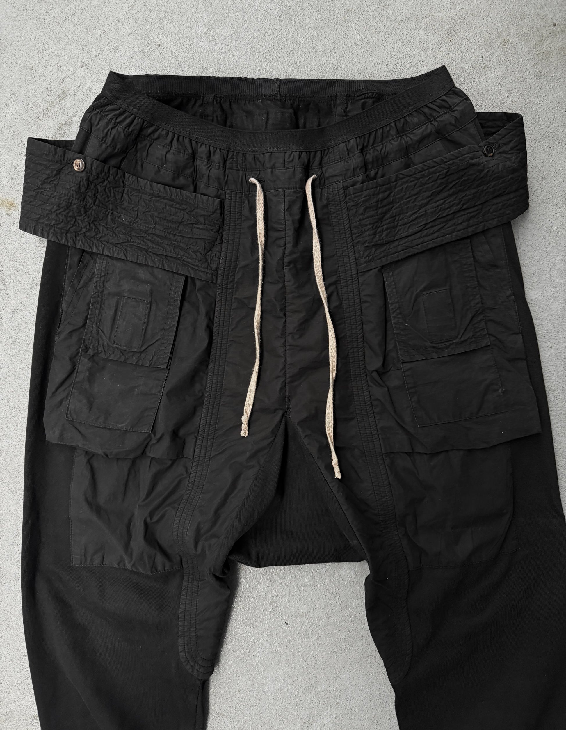 Black cargo pants with multiple pockets and drawstring on a gray background
