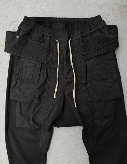 Black cargo pants with multiple pockets and drawstring on a gray background