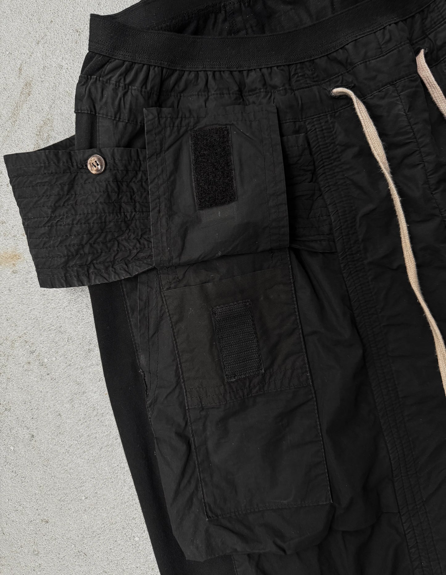 Close-up of black cargo pants with a visible brand logo on a light gray background