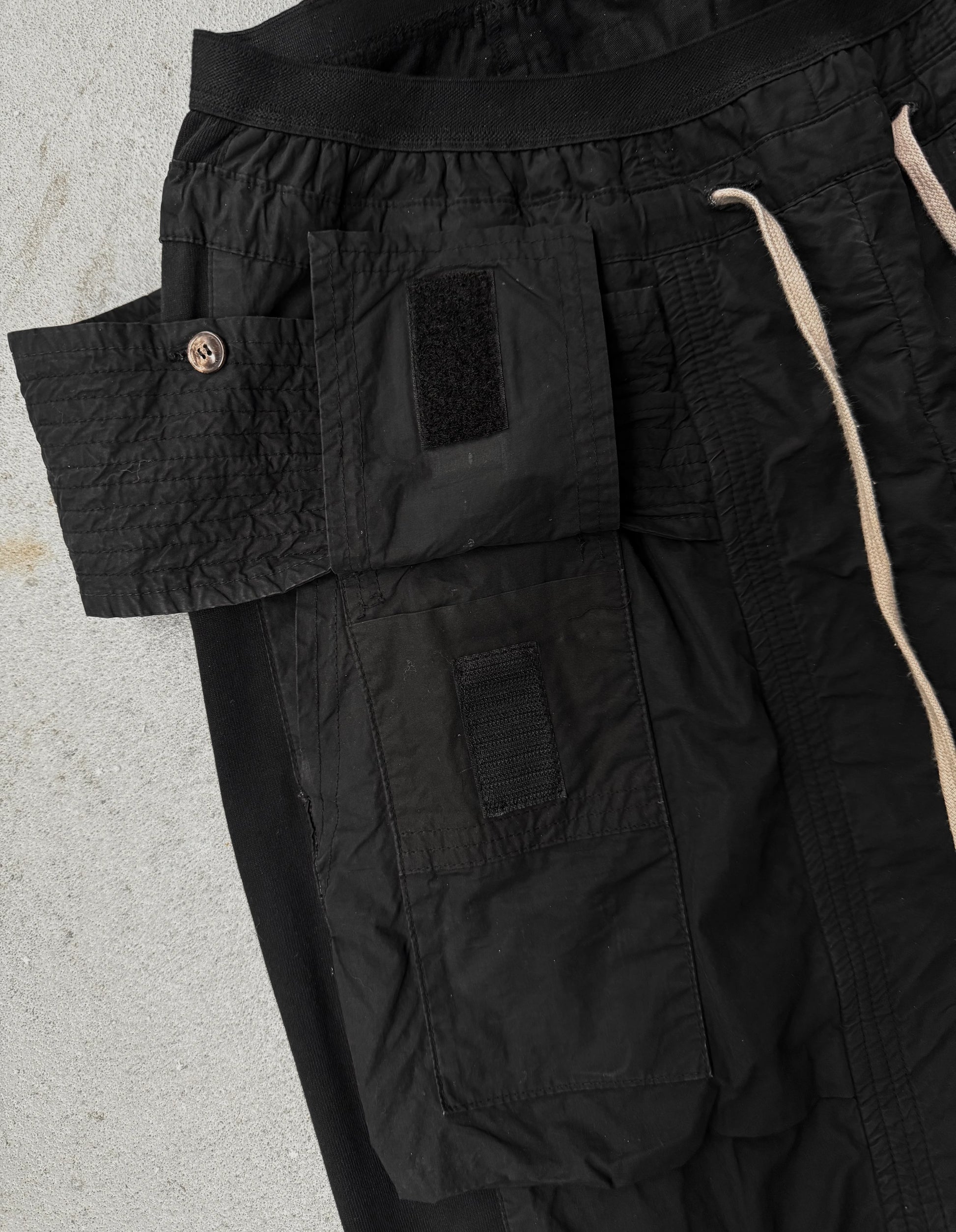 Close-up of black cargo pants with a visible brand logo on a light gray background