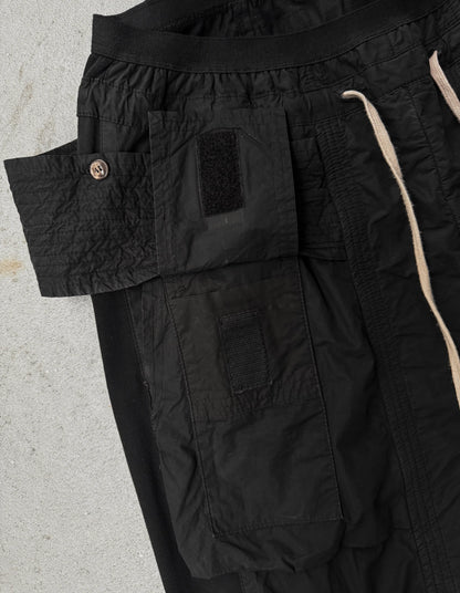 Close-up of black cargo pants with a visible brand logo on a light gray background