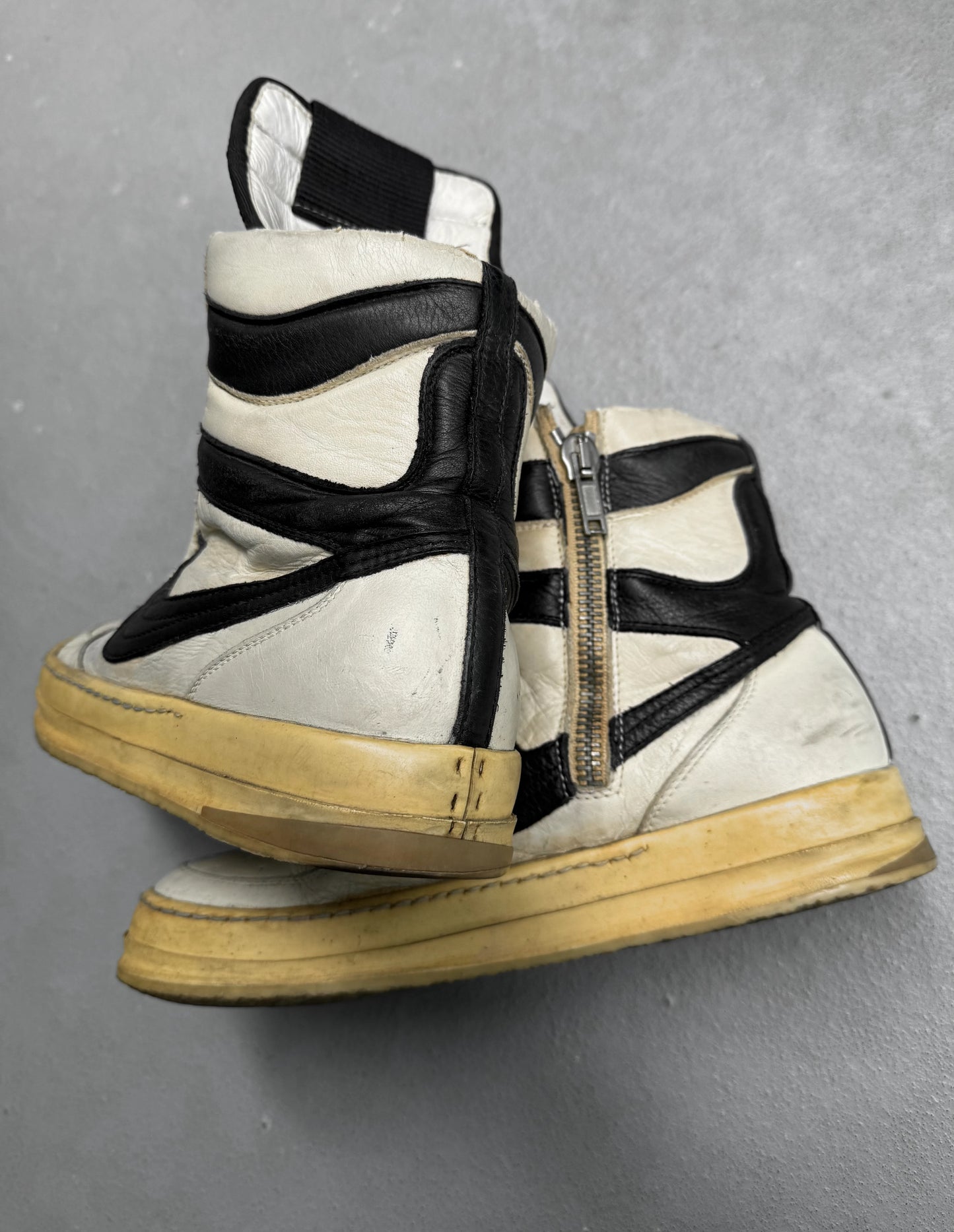 White high-top sneakers with black straps and a gold zipper on a gray background