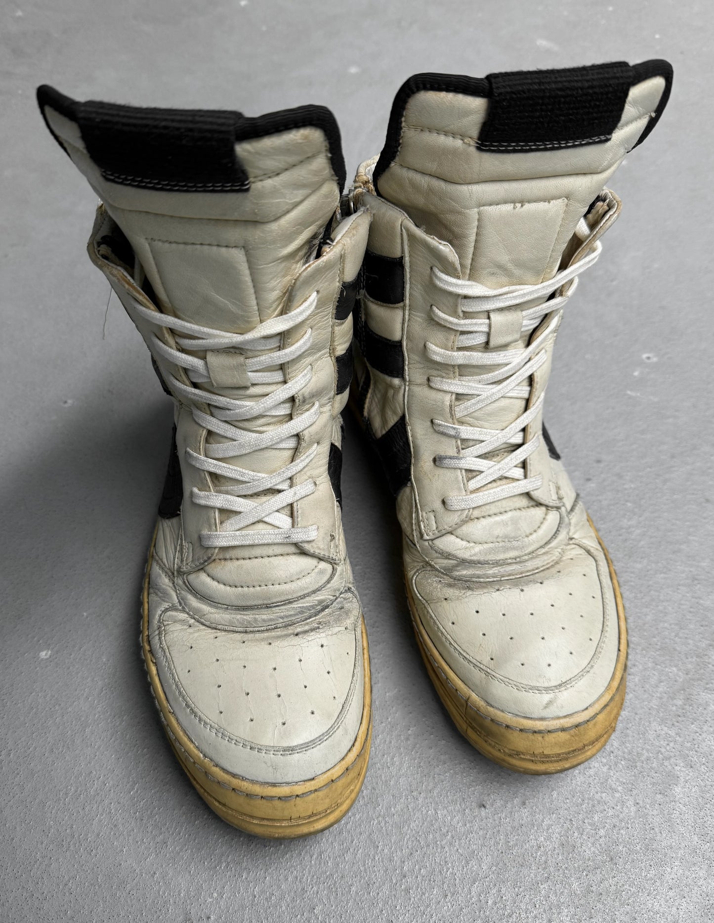 Pair of worn white and beige combat boots on a gray surface