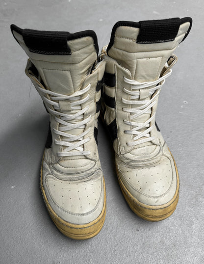 Pair of worn white and beige combat boots on a gray surface