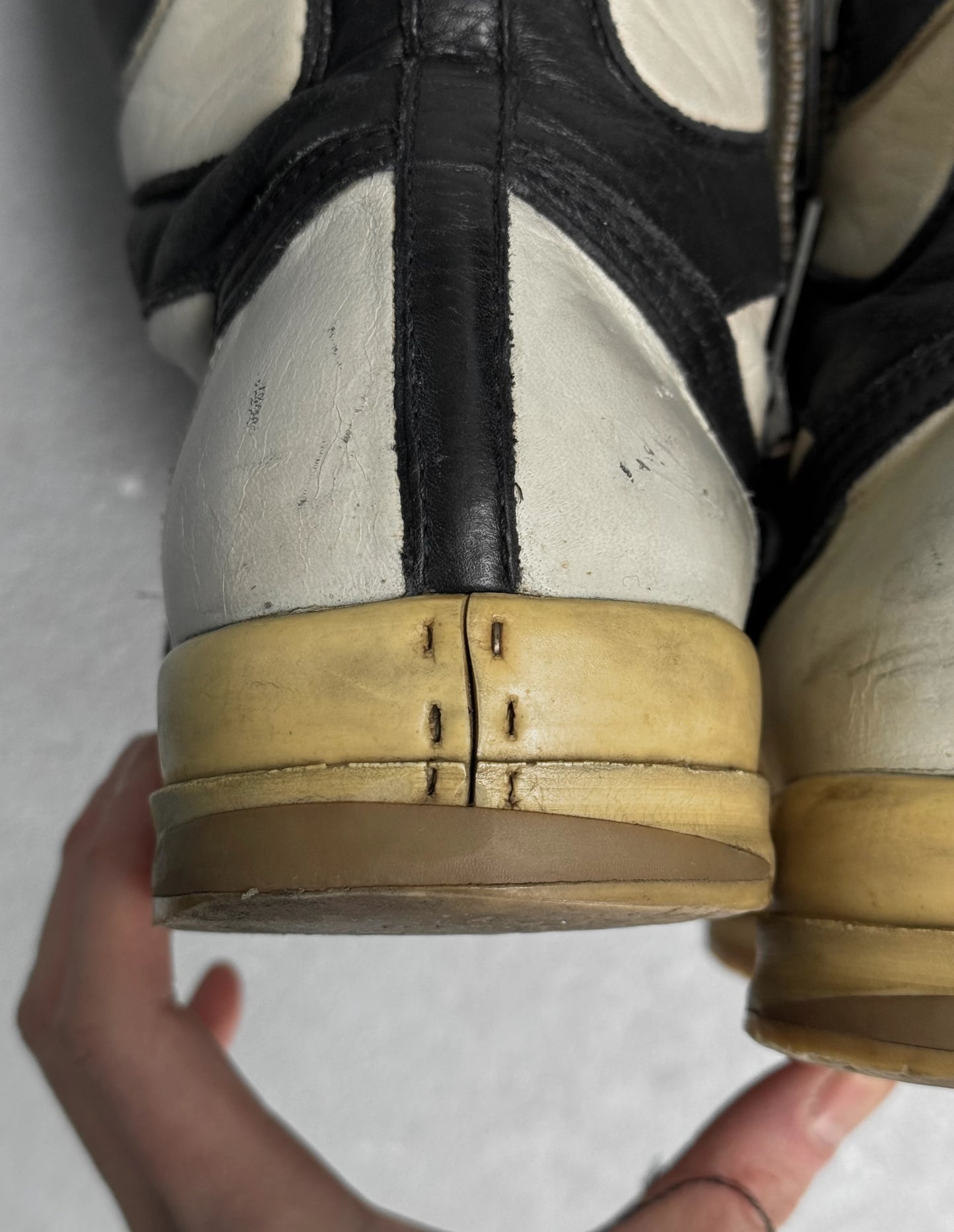 Close-up of a worn shoe with a hand holding it, on a light background