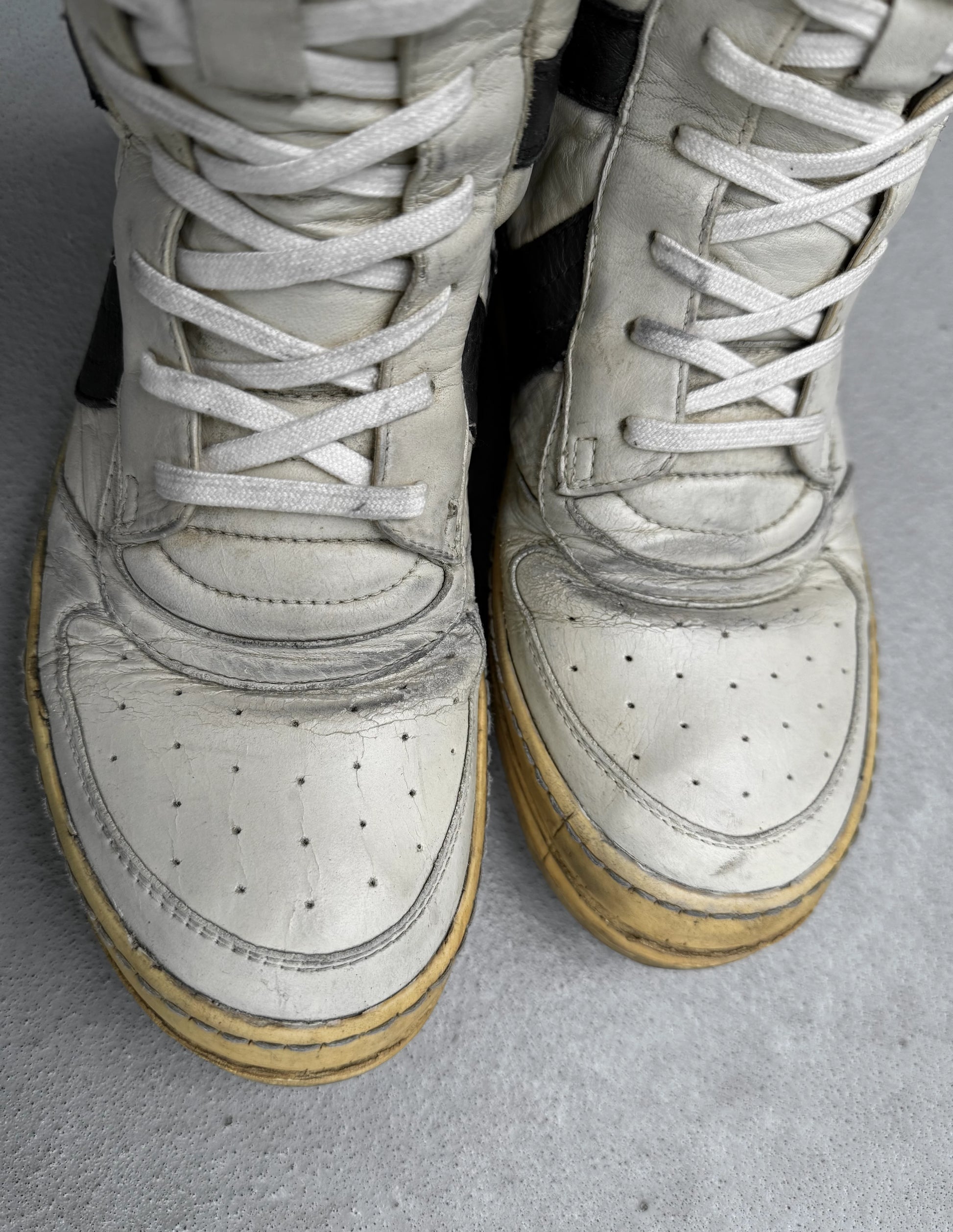 Pair of white high-top sneakers with brown soles on a gray surface