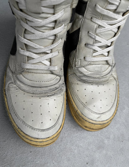 Pair of white high-top sneakers with brown soles on a gray surface