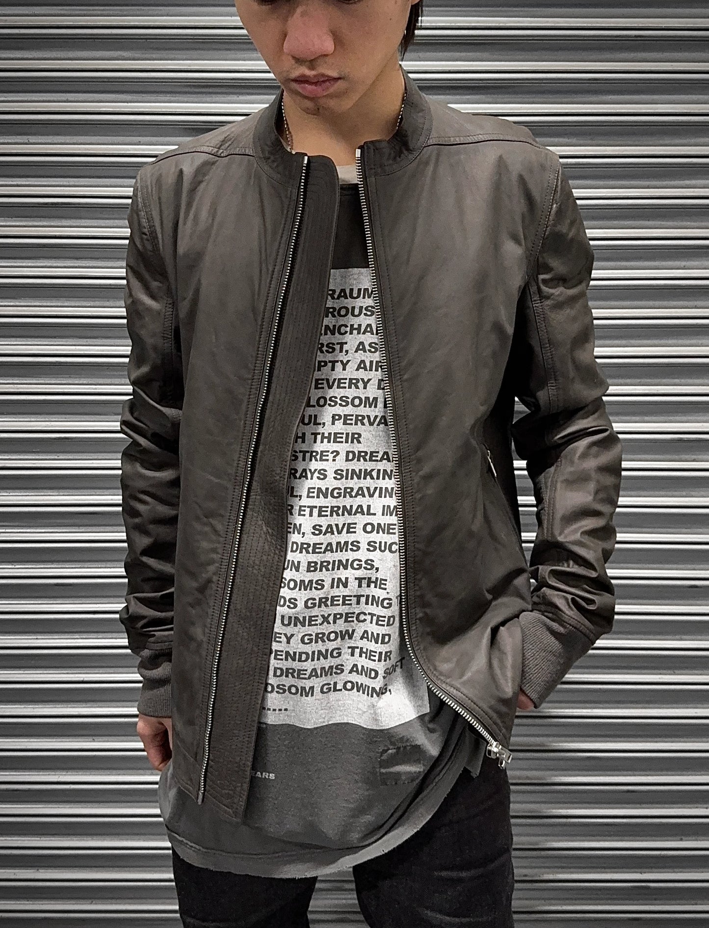 Person wearing a gray jacket over a graphic t-shirt with text, standing in front of a metallic shutter.