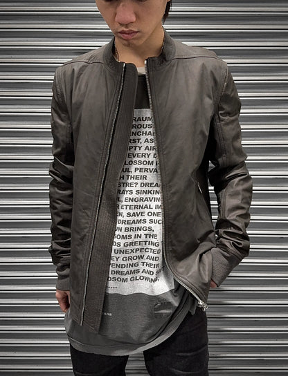 Person wearing a gray jacket over a graphic t-shirt with text, standing in front of a metallic shutter.