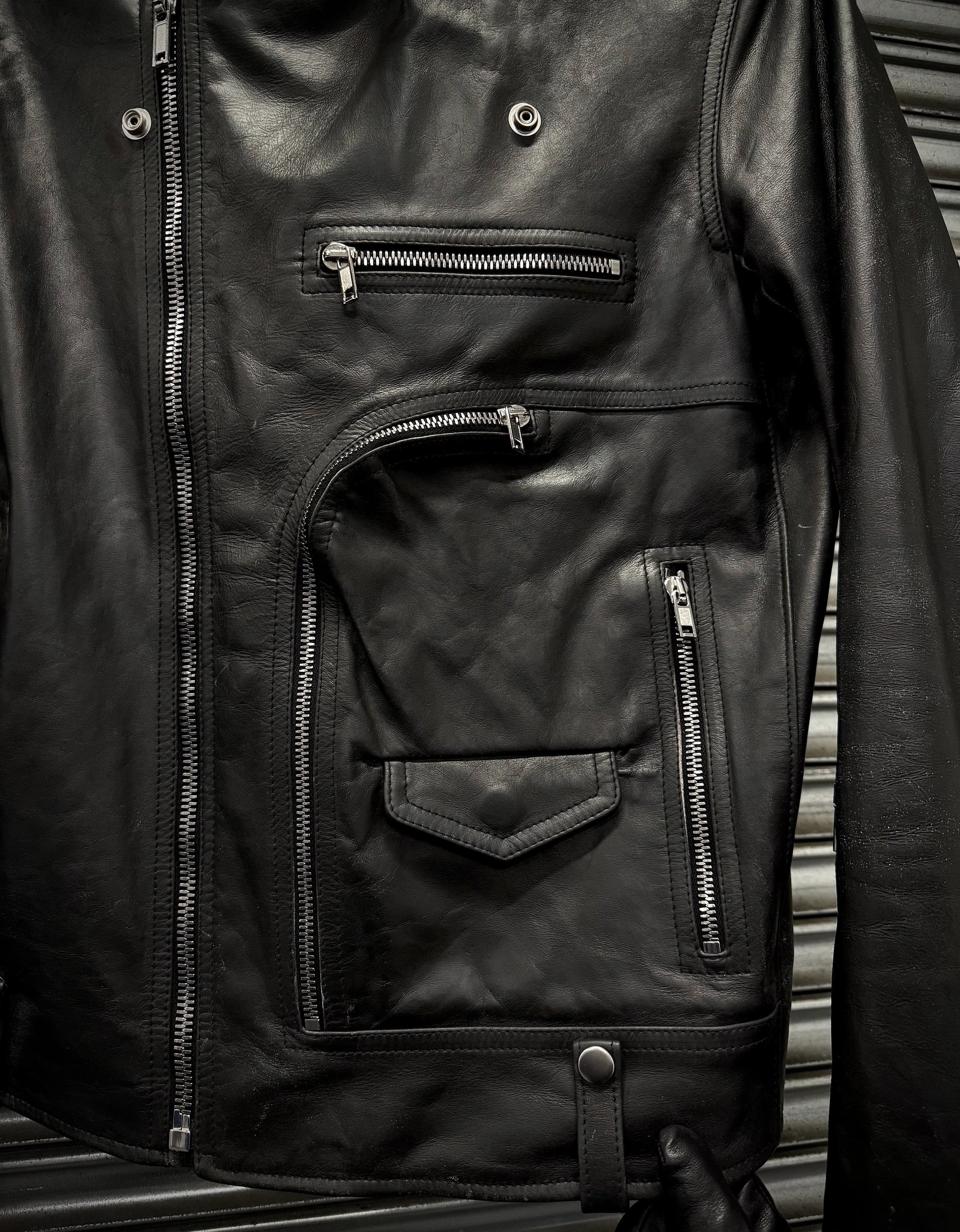 Close-up of a black leather jacket with zippers on a metallic surface