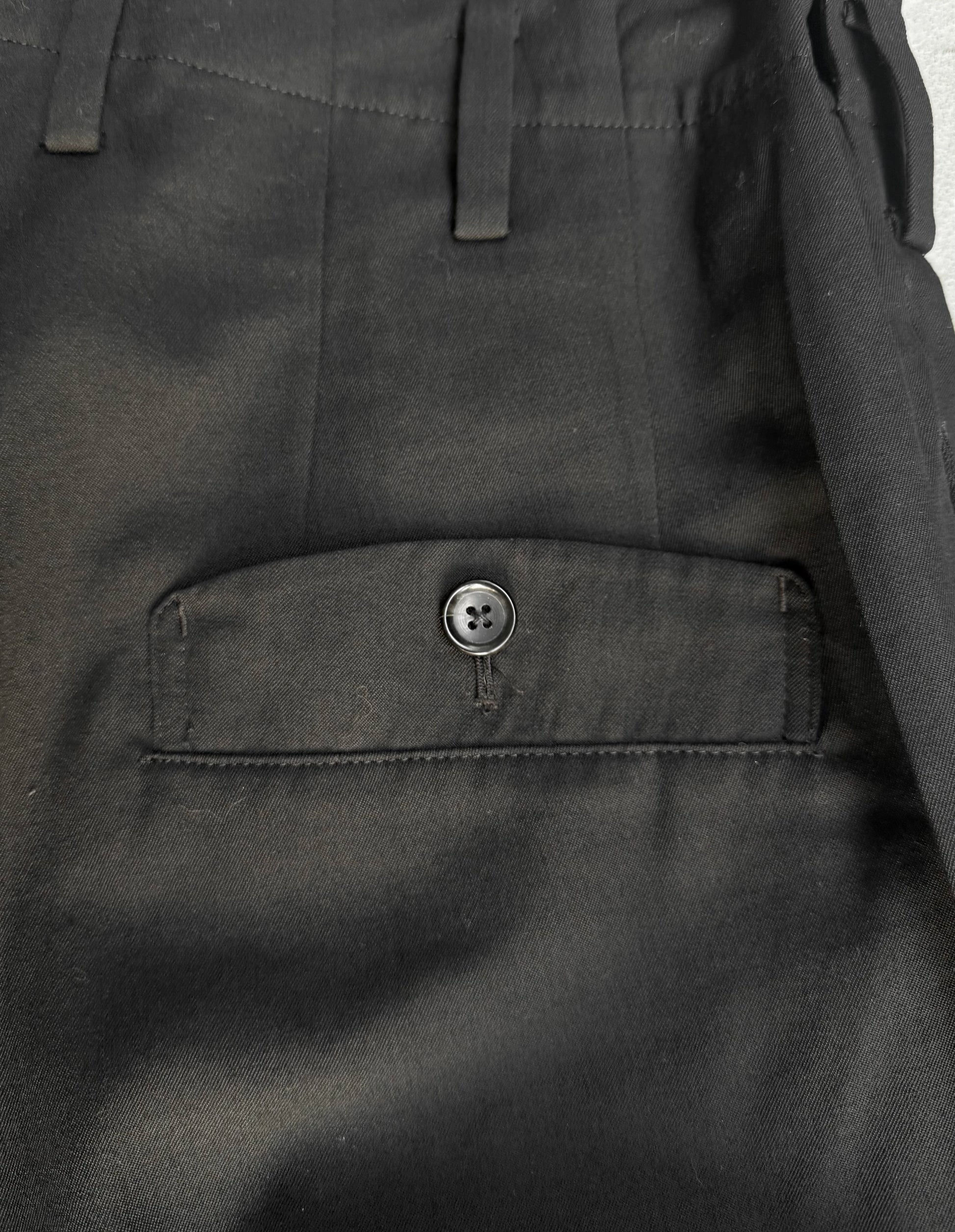 Close-up of dark gray pants with a button on a plain background
