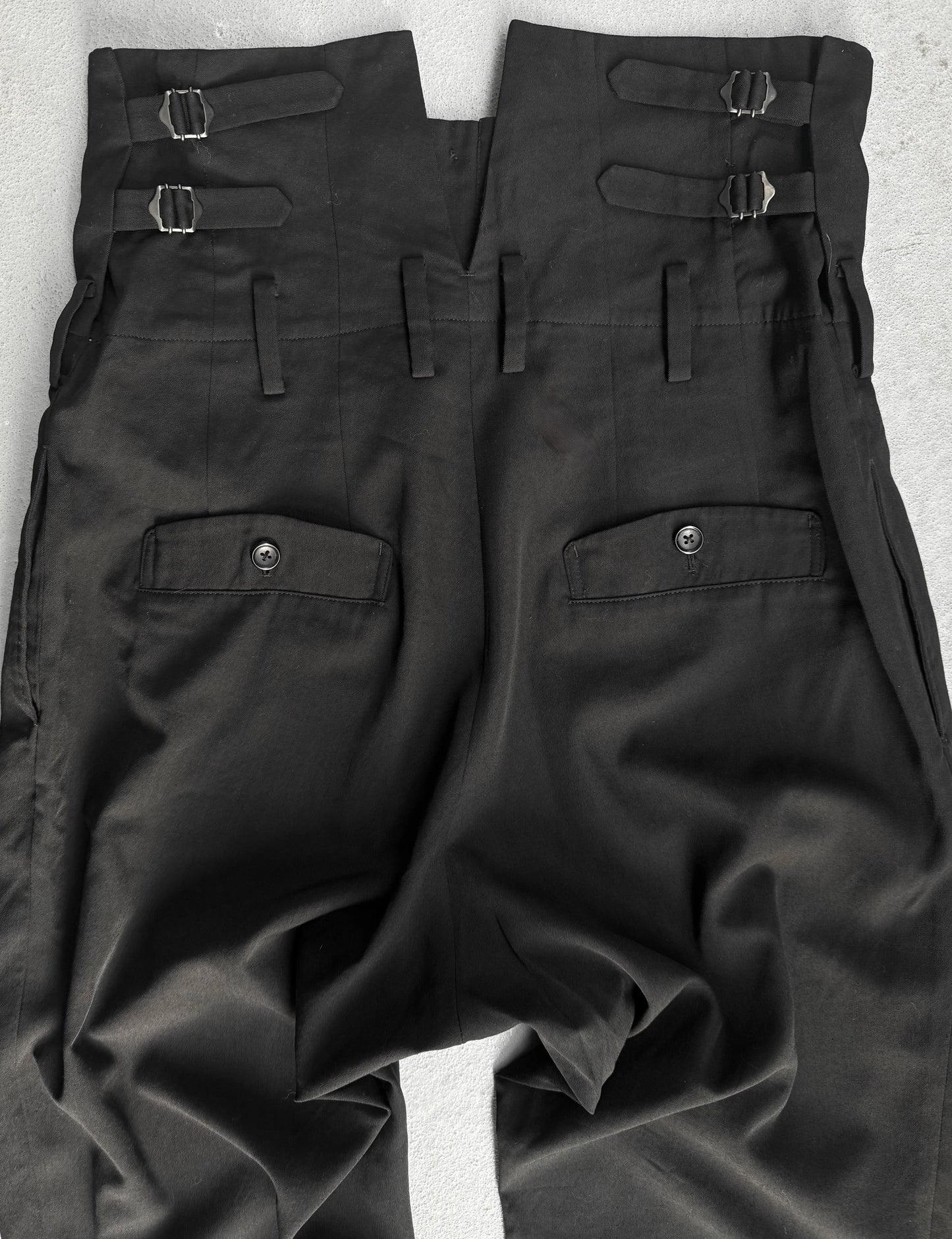 Black pants with multiple pockets and straps on a light gray background
