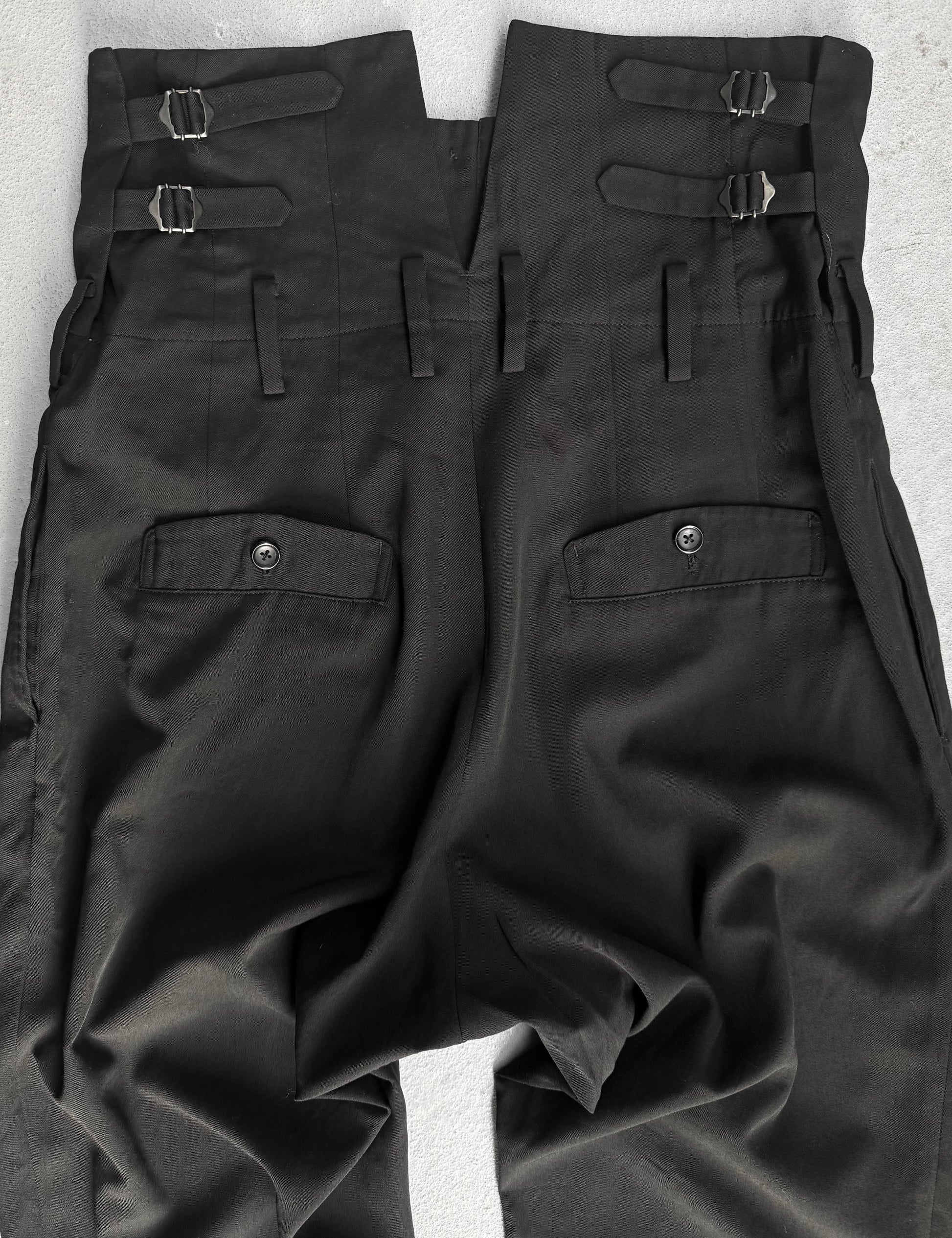 Black pants with multiple pockets and straps on a light gray background