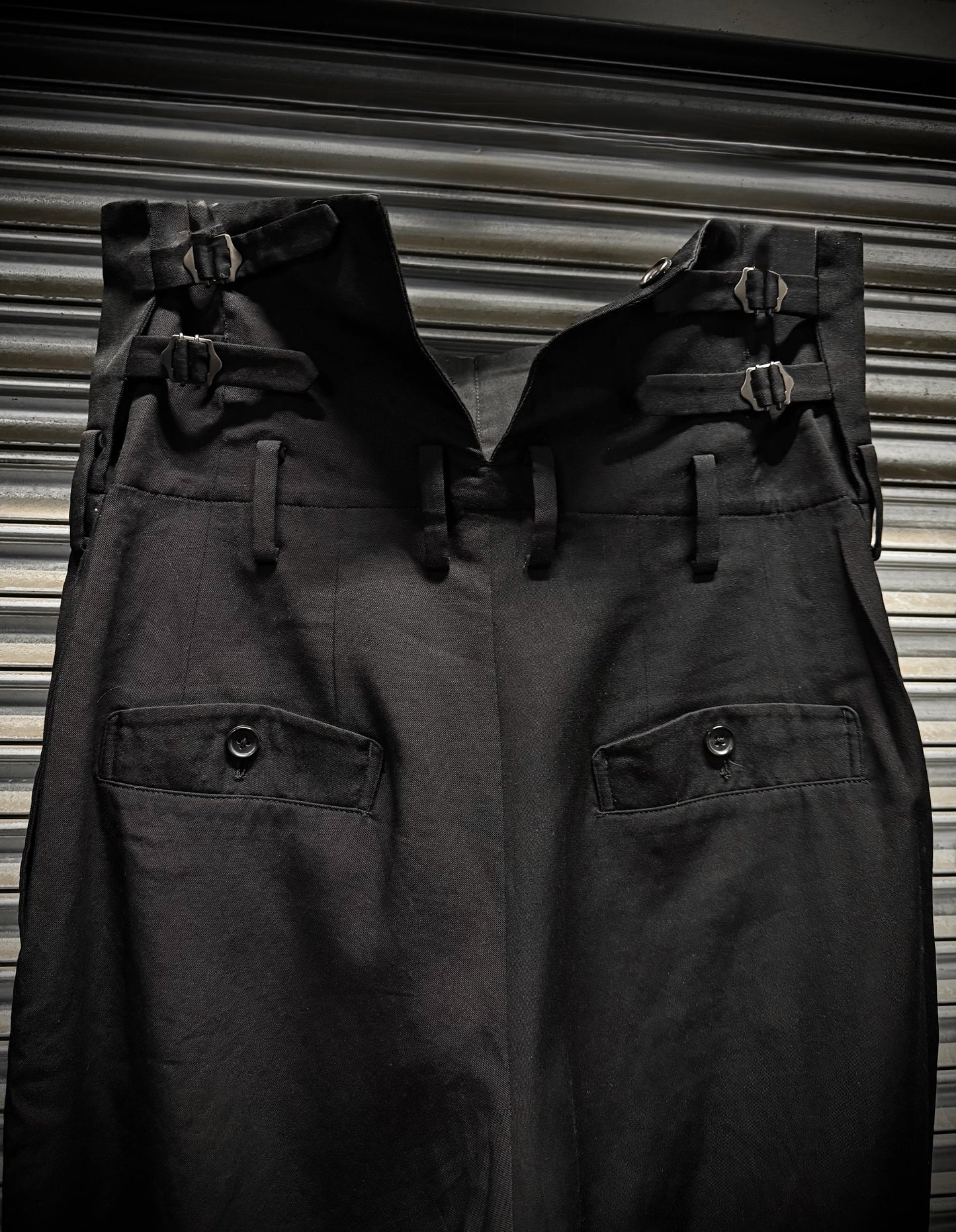 Two pairs of dark pants with buckles on a striped background