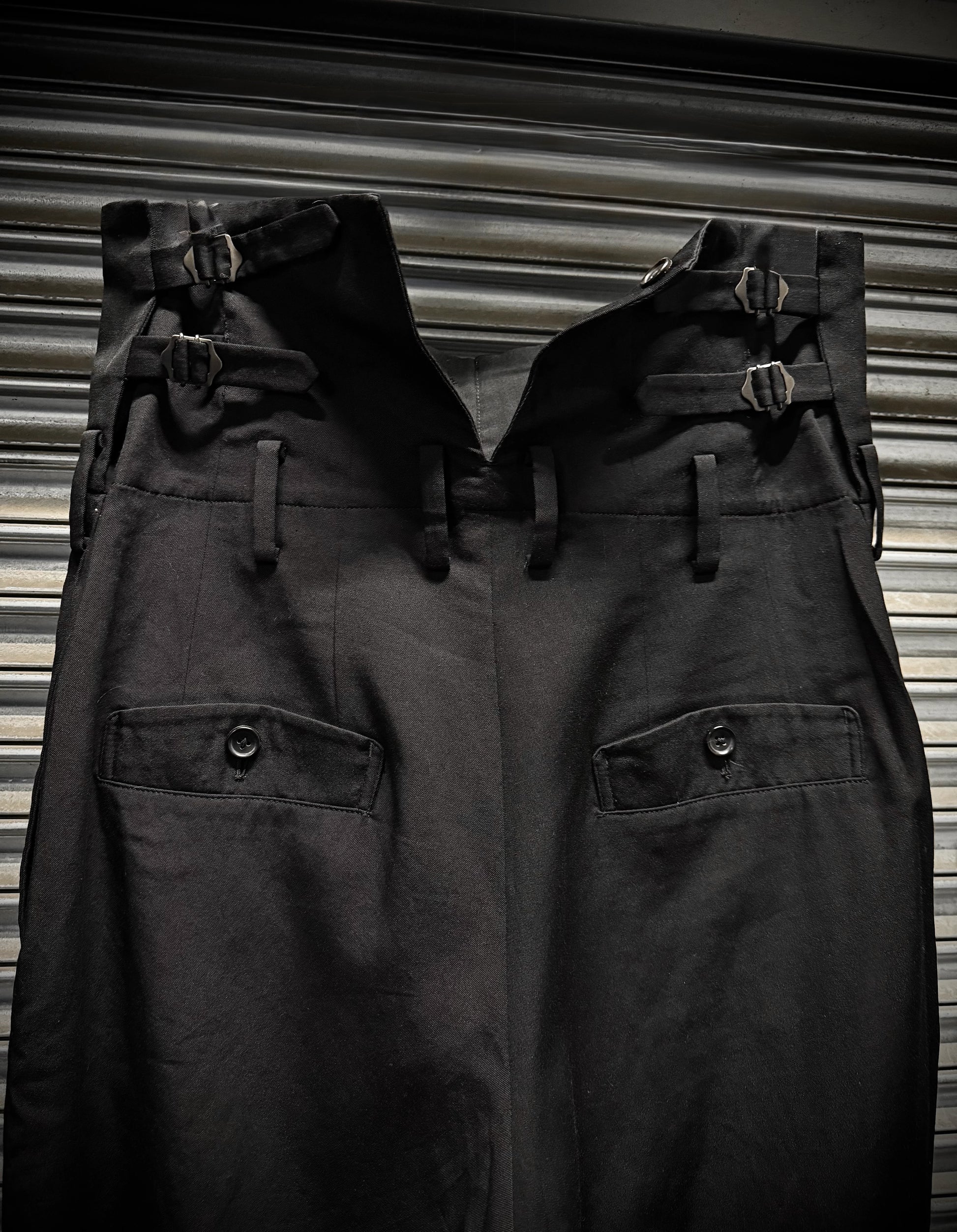 Two pairs of dark pants with buckles on a striped background