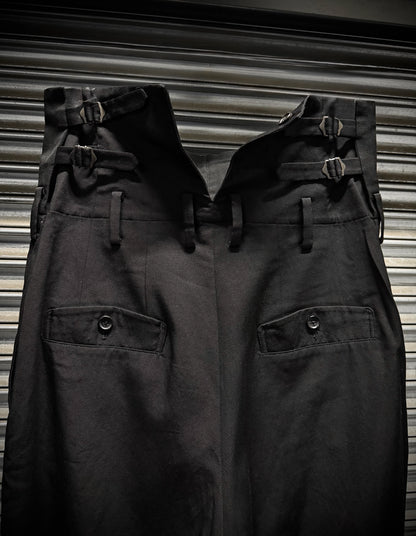 Two pairs of dark pants with buckles on a striped background