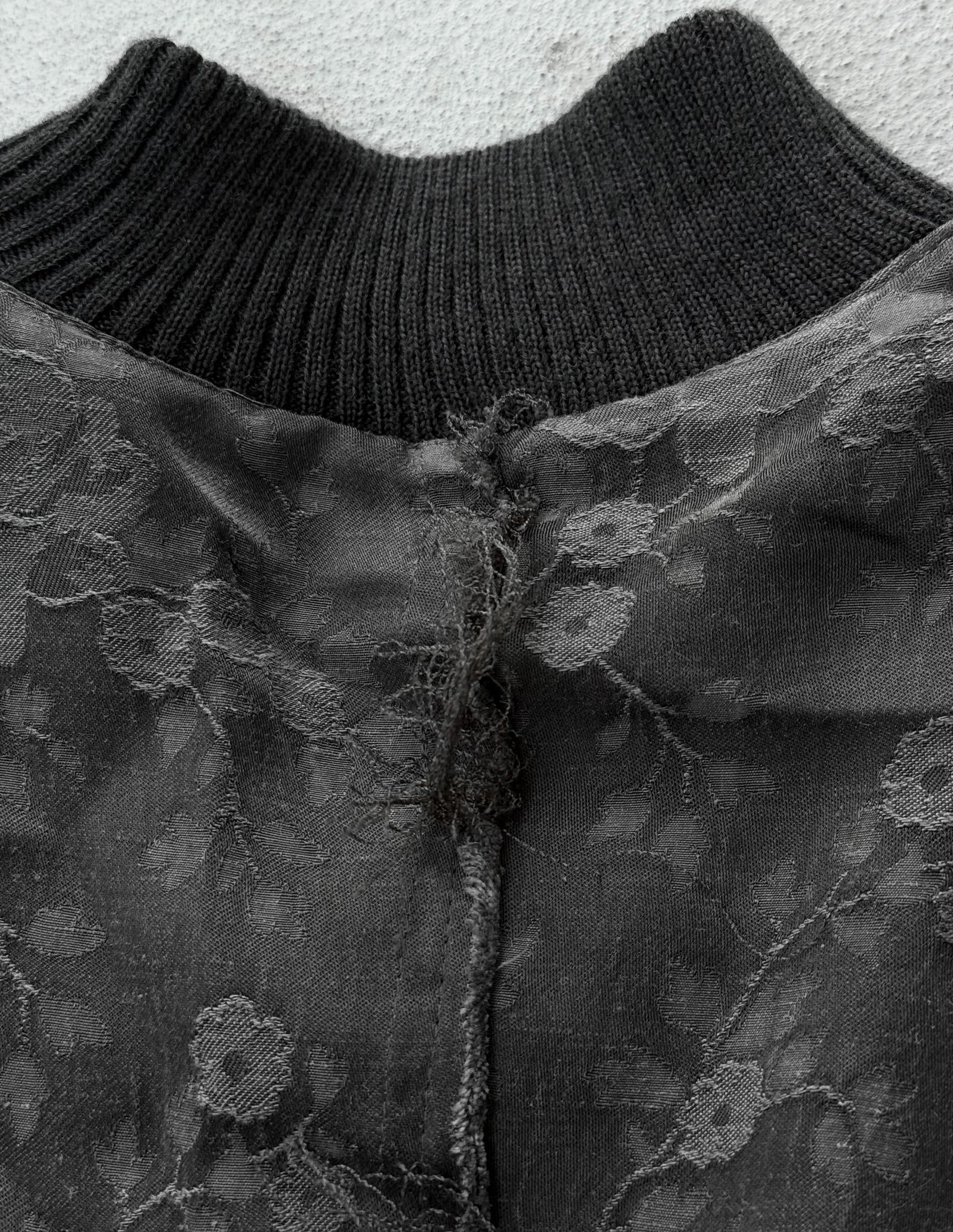 Close-up of a black knit sweater with floral lace trim against a light background