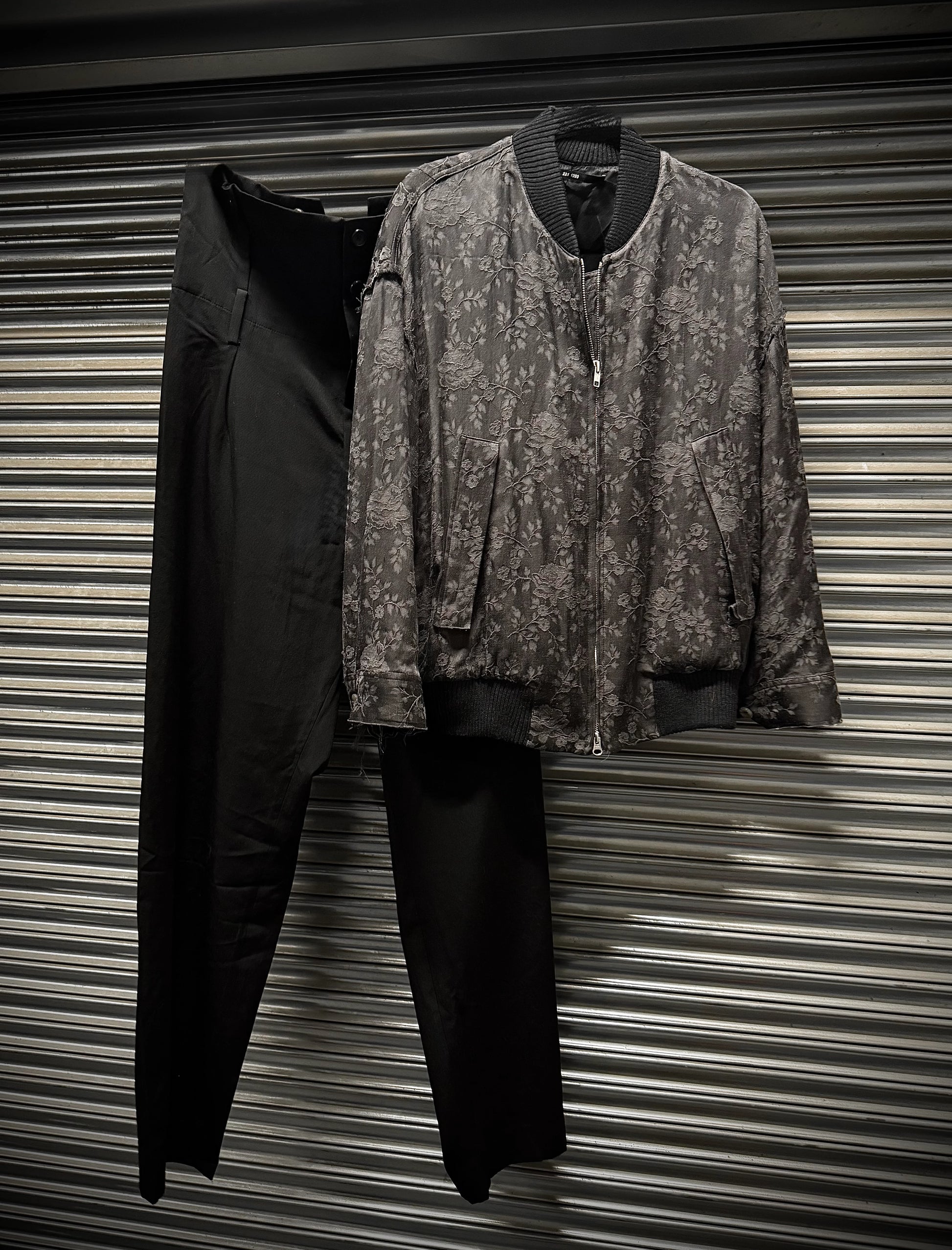 Two jackets, one black and one patterned, hanging against a corrugated metal background.