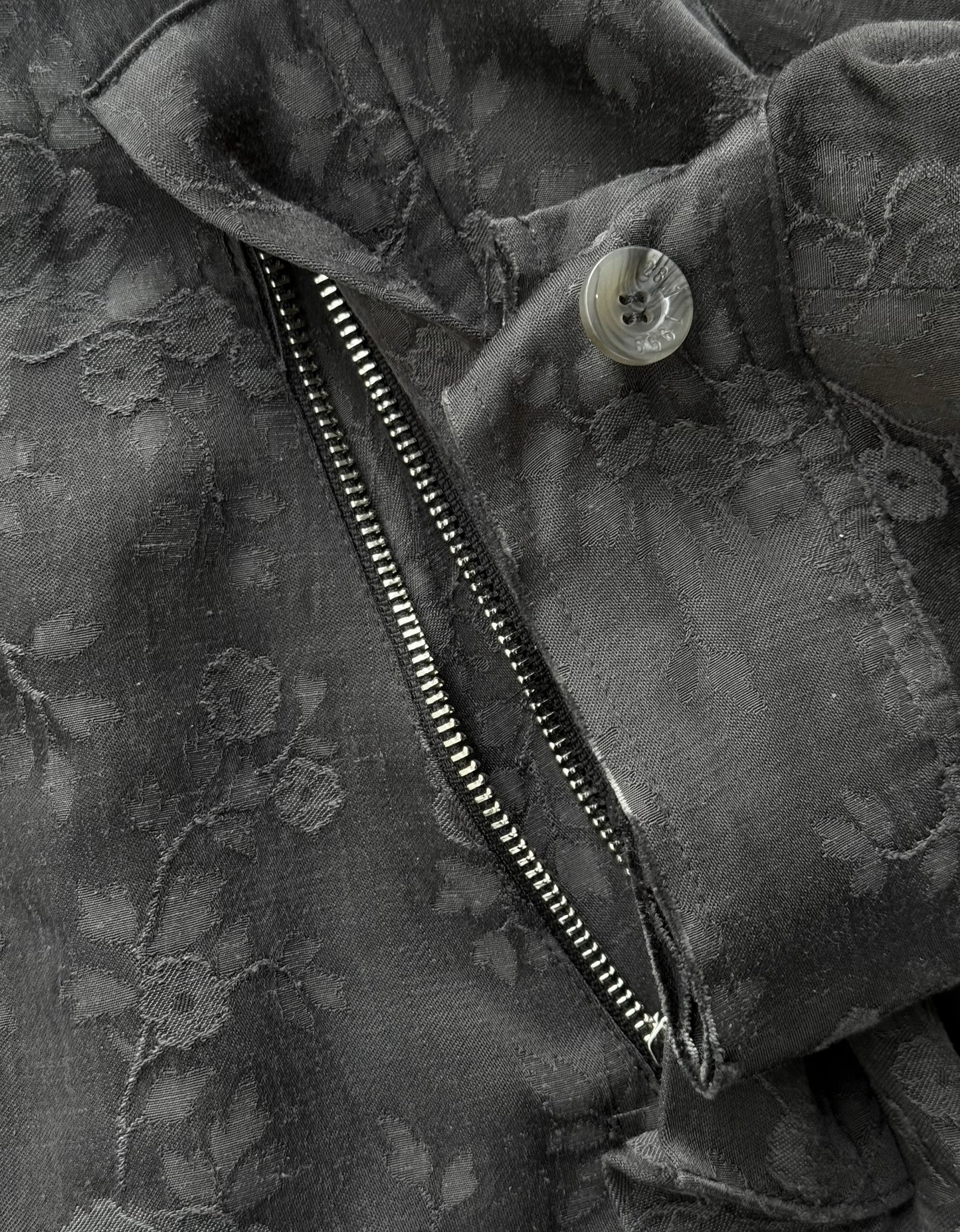 Close-up of a black floral-patterned jacket with a zipper and button.