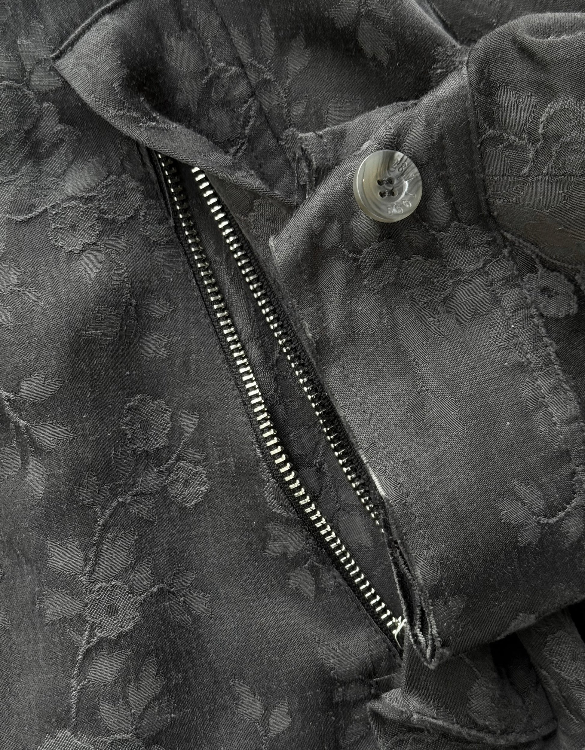 Close-up of a black floral-patterned jacket with a zipper and button.