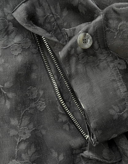 Close-up of a black floral-patterned jacket with a zipper and button.