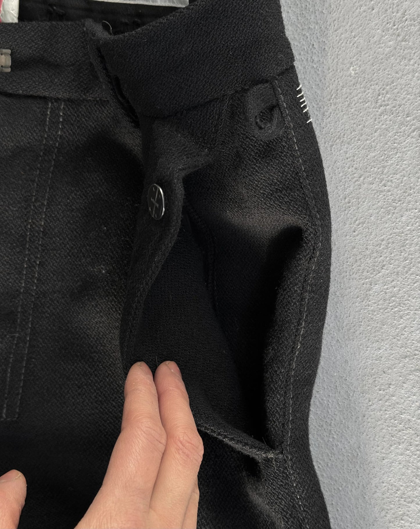 Close-up of black pants with a hand touching the fabric against a gray background