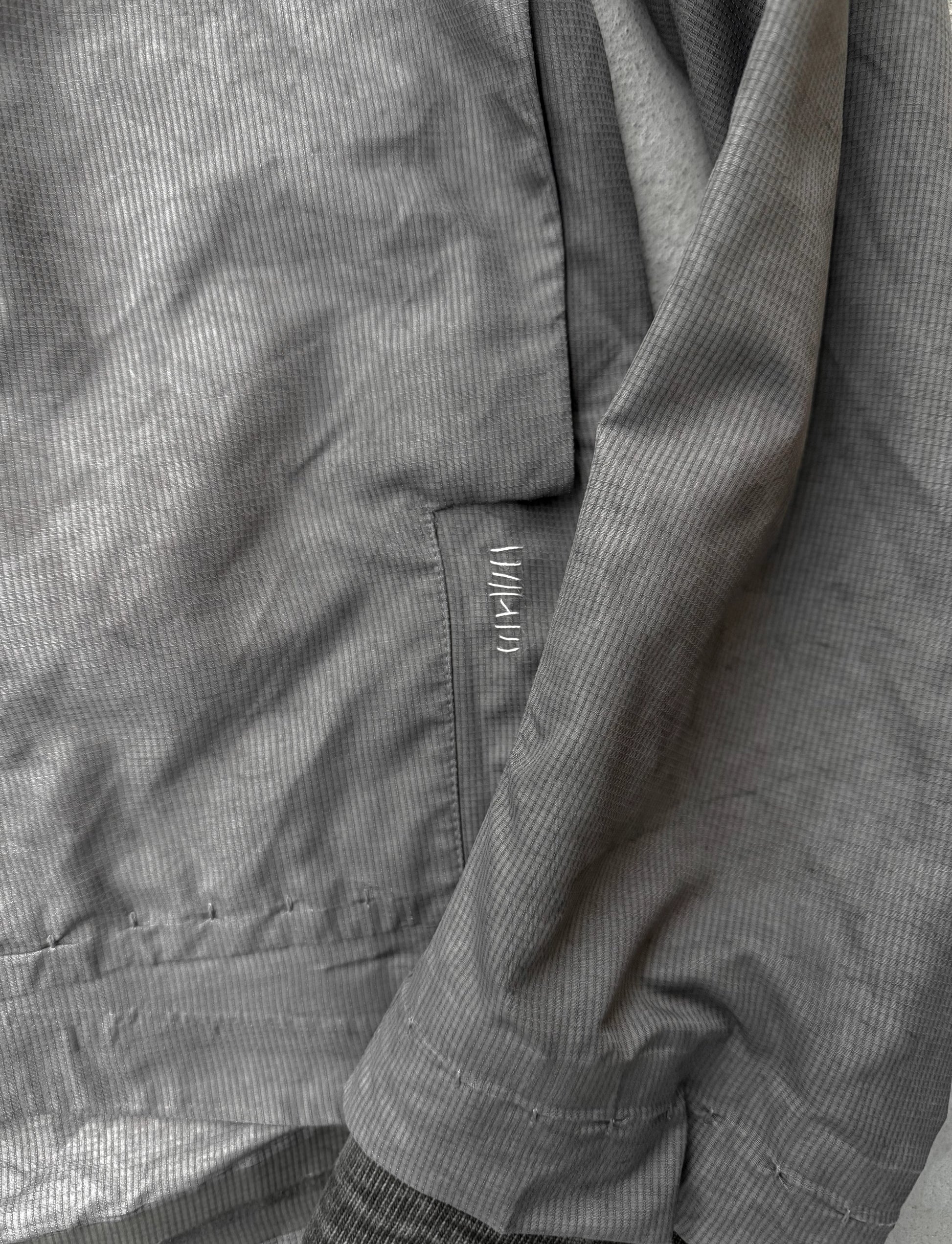 Close-up of a gray jacket with a brand logo on the chest pocket.