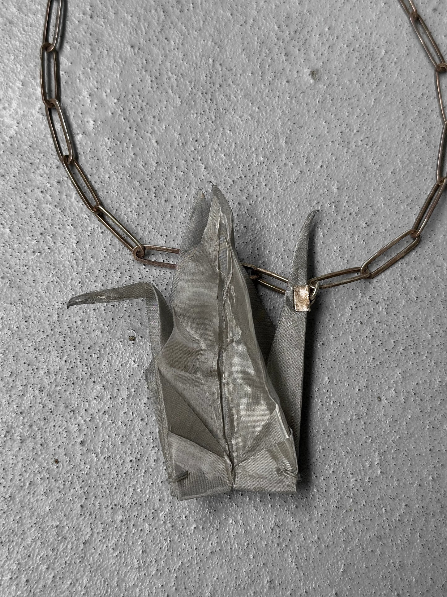 Silver origami crane pendant on a chain against a gray concrete background
