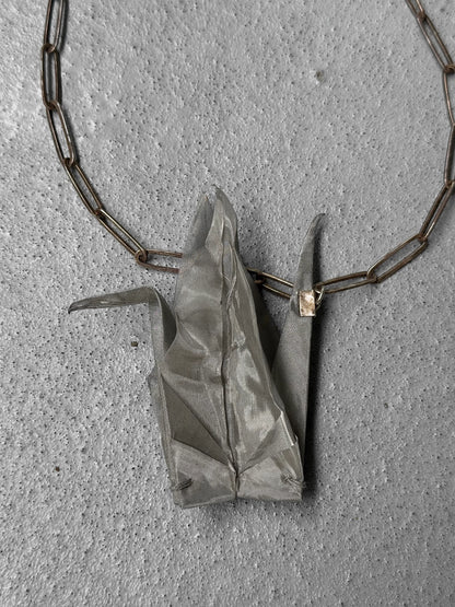 Silver origami crane pendant on a chain against a gray concrete background