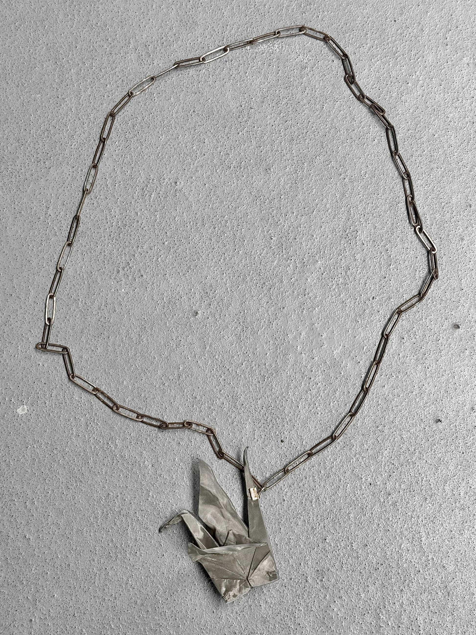 Necklace with a silver chain and origami crane pendant on a light gray background