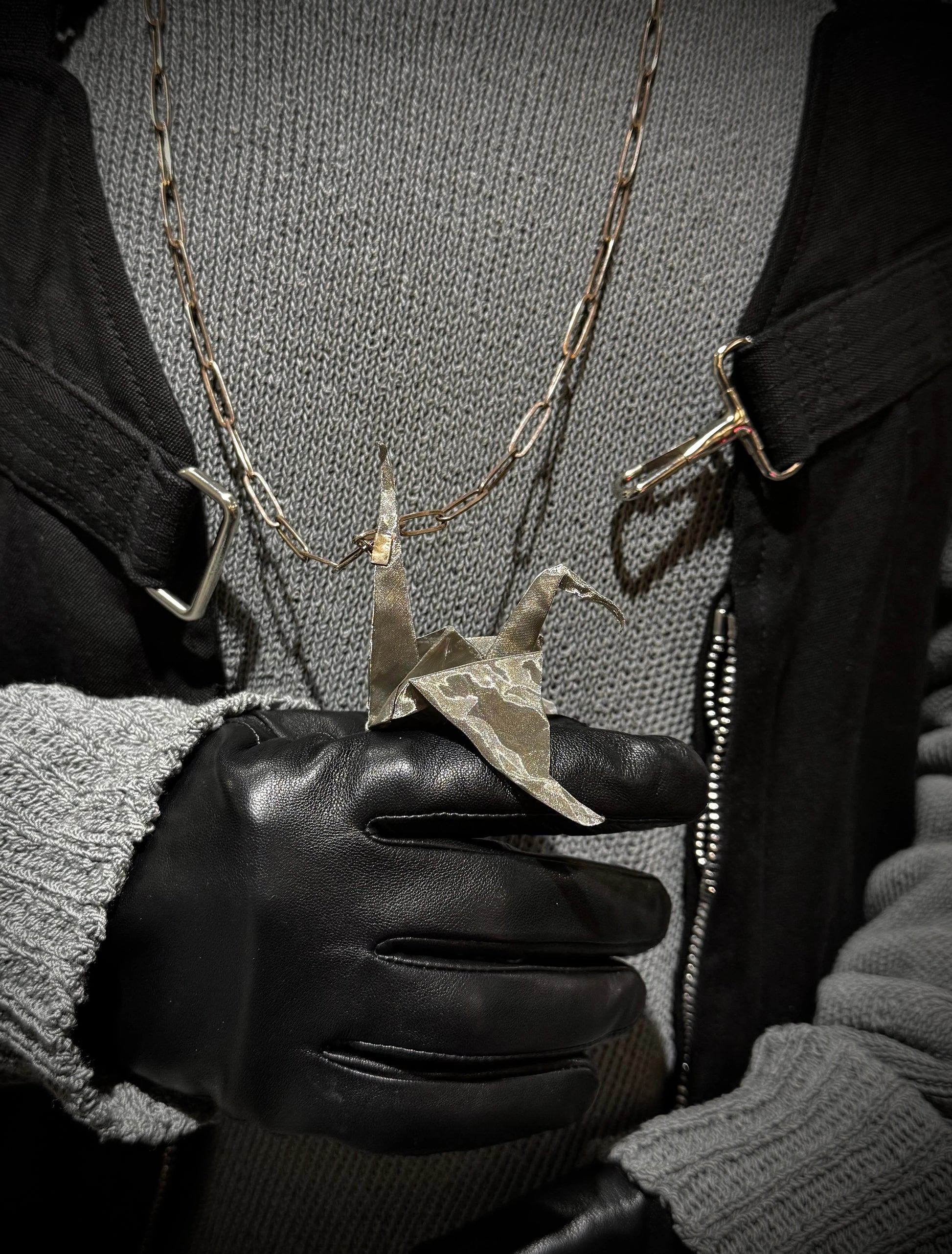 Person wearing a black glove holding a necklace with a unique pendant.