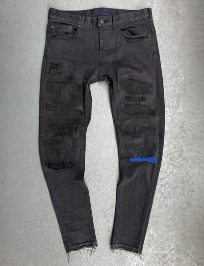 Black distressed jeans with a brand logo on a gray background