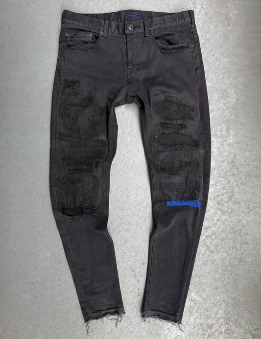 Black distressed jeans with a brand logo on a gray background