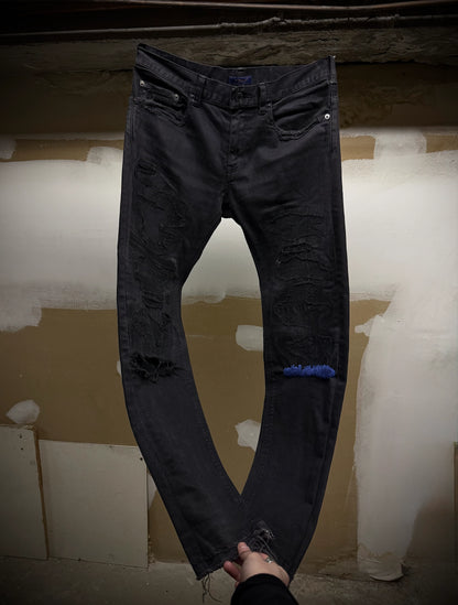 Black distressed jeans held up against a plain background