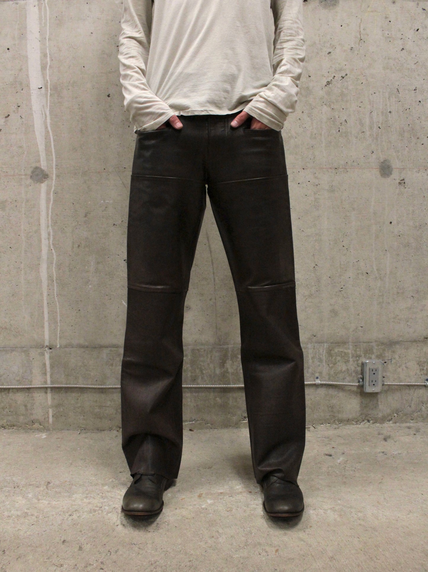 Person wearing black pants and a light gray long-sleeve shirt against a concrete wall.