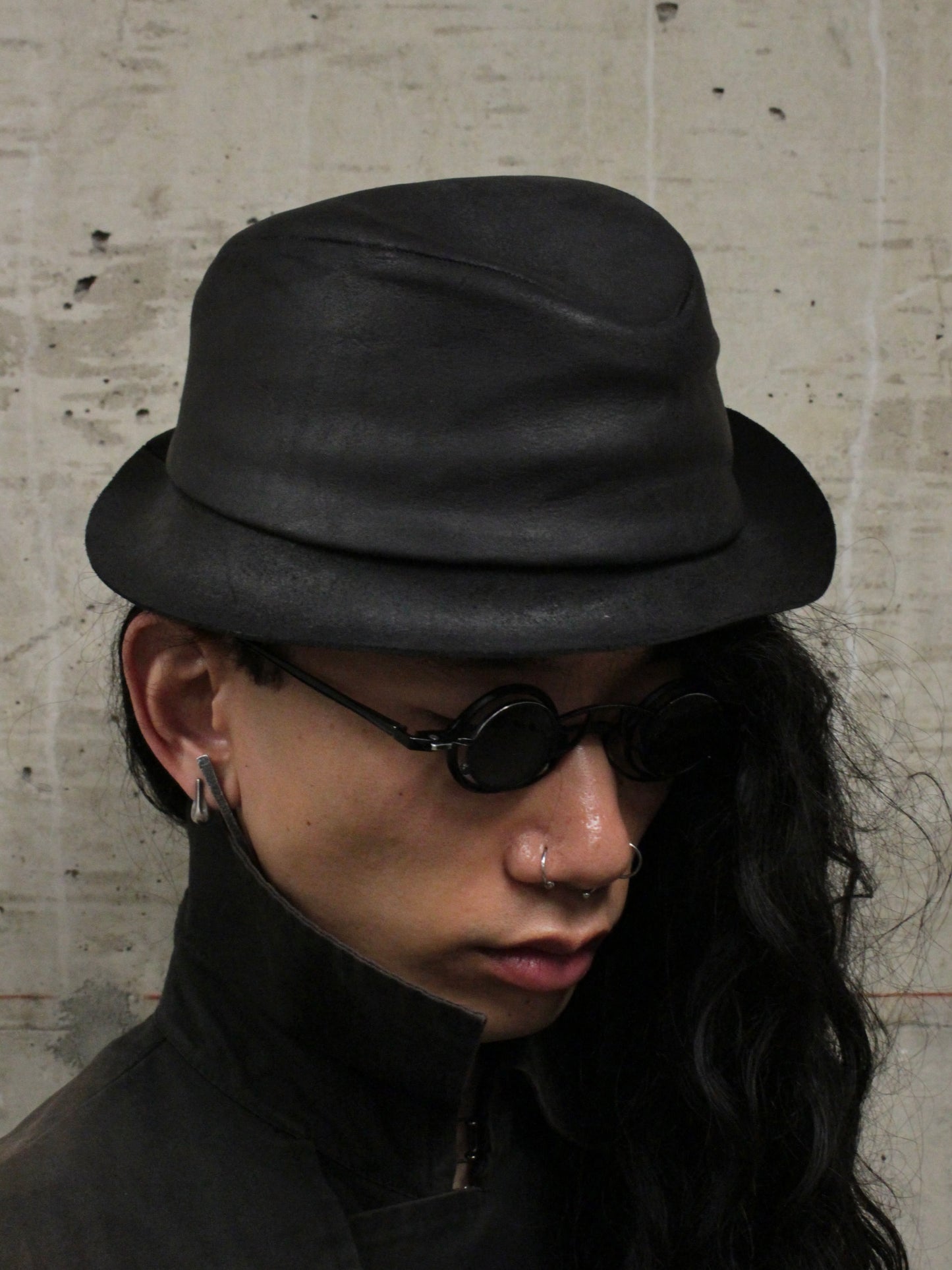 Person wearing a black hat and sunglasses against a textured wall.