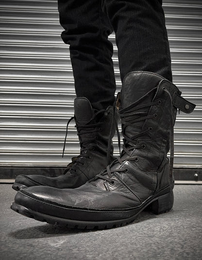 Black leather boots worn with black pants against a metallic background