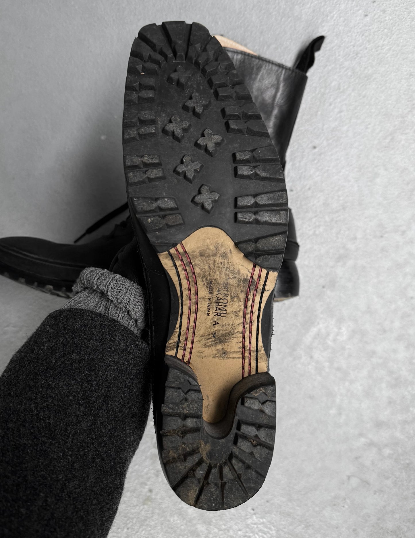 Close-up of a black leather shoe with a worn sole on a gray surface